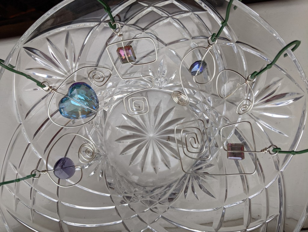 hanging ornaments made from faceted glass beads and spirals of silver-coloured wire arranged around the rim of a crystal glass bowl
