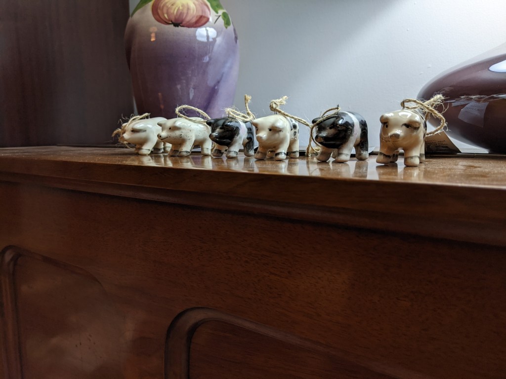 Six small ceramic pigs with loops on their backs for hanging, lined up under a lamp