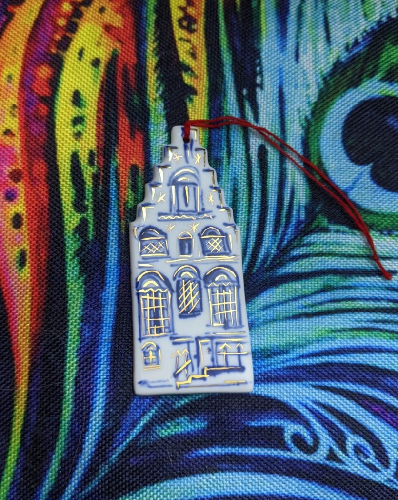 Flat ceramic Christmas tree decoration representing a tall house with Dutch gables, with doors and windows picked out in blue and gilt