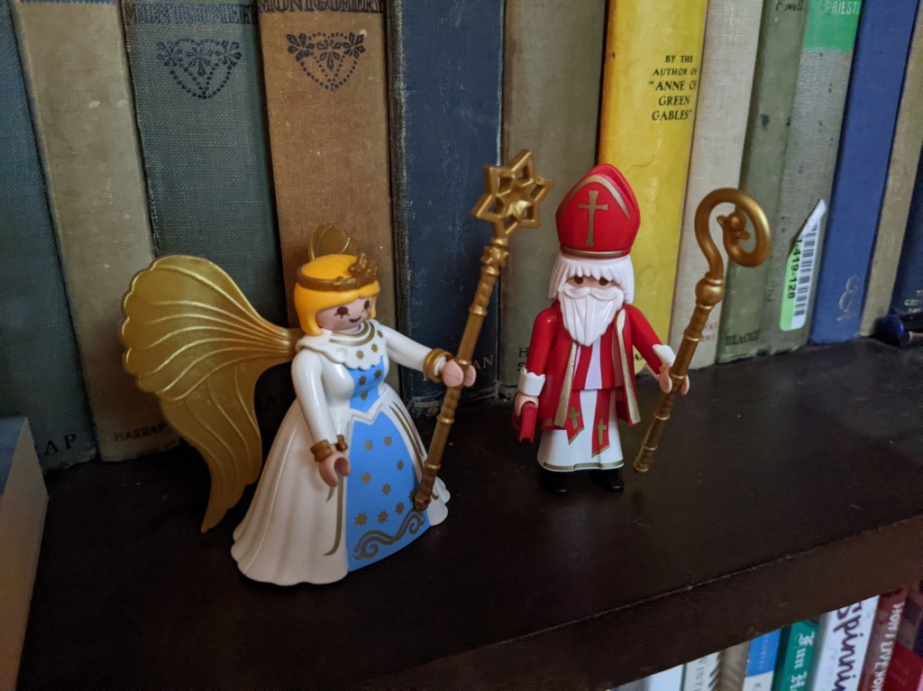 Playmobil figures of an angel with a wide crinoline skirt and floor-length gold wings, and a man with a white beard and red bishop's mitre and robes