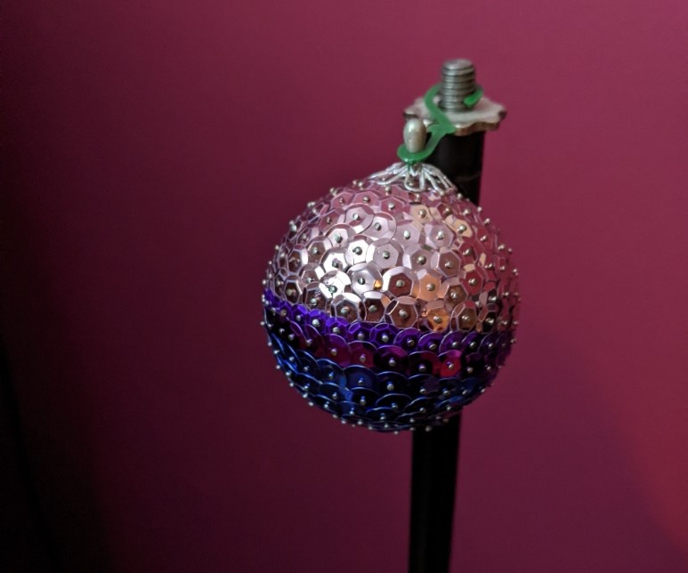 A bauble covered in sequins arranged in stripes of pink, purple and blue