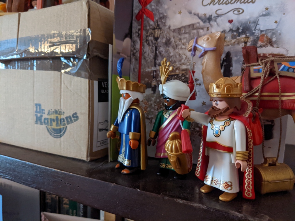 Playmobil figures representing the three kings plus camel surveying a scene dominated by a cardboard shoebox