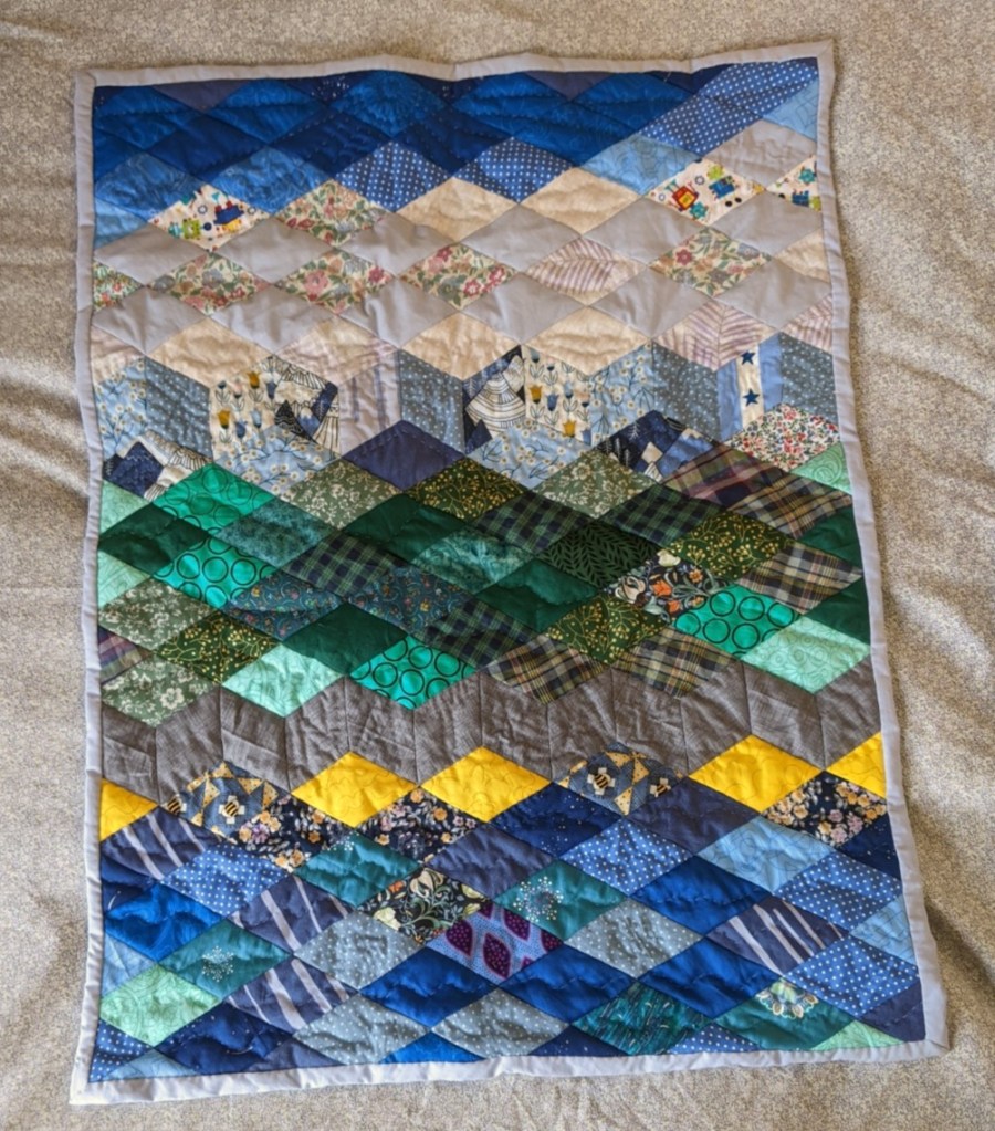 Cot quilt in patchwork diamonds, mostly blues and greens.
