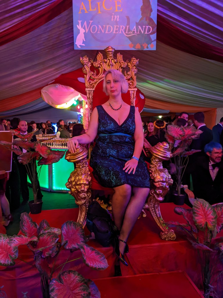 A woman in a cocktail dress sits in an elaborate gilt chair 