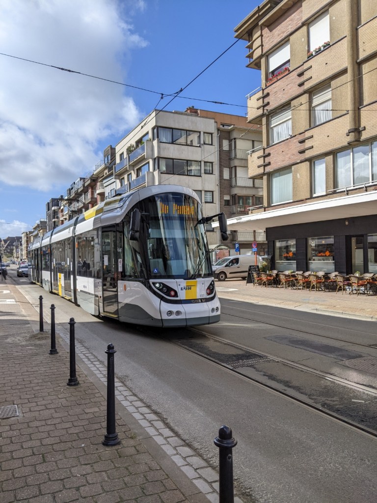 A tram runs down the middle of a street lined with boxy blocks of flats 