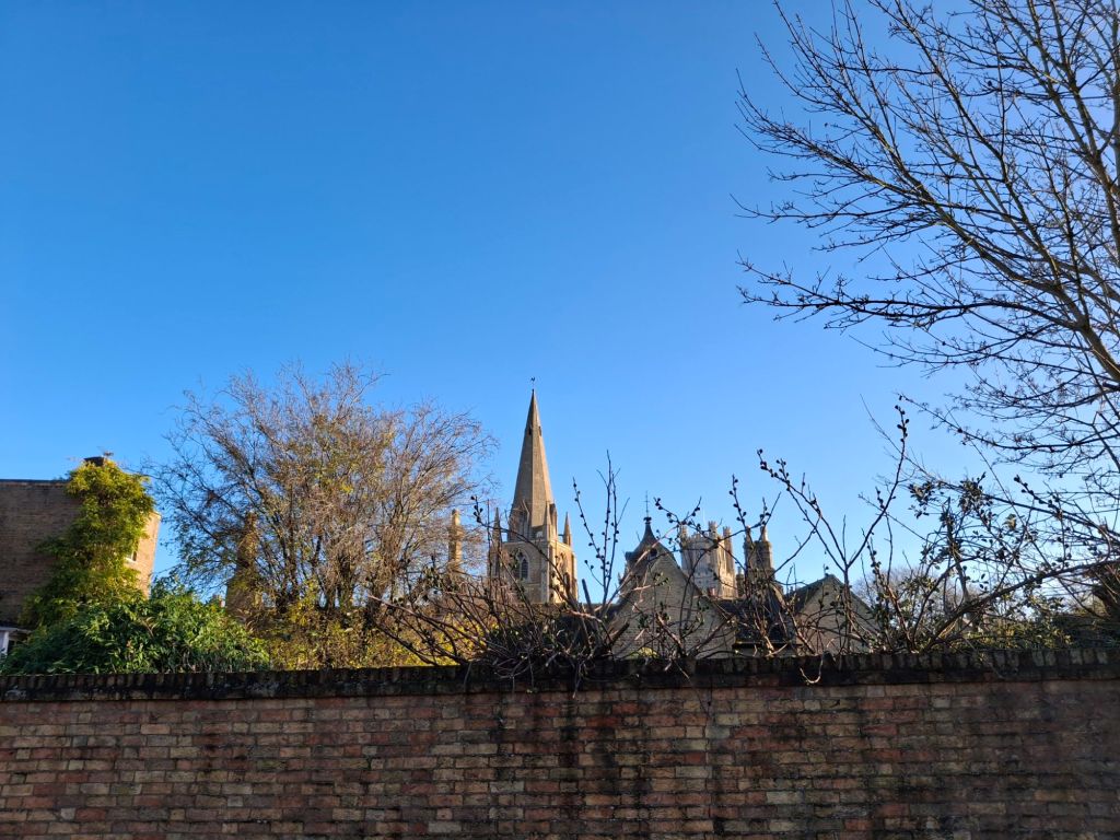 An assortment of towers and spires seen beyond the top of a high yellow brick wall against a clear blue sky