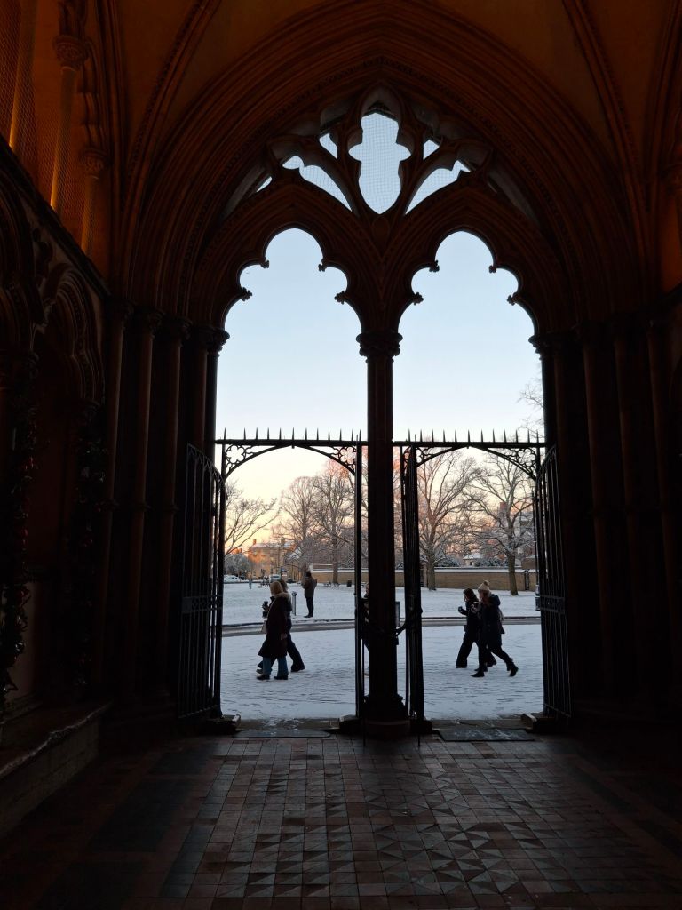 Snowy scene with people walking past a Gothic doorway 