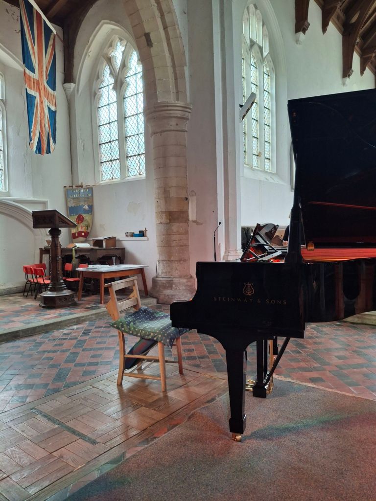 A very glossy grand piano stands in a whitewashed church