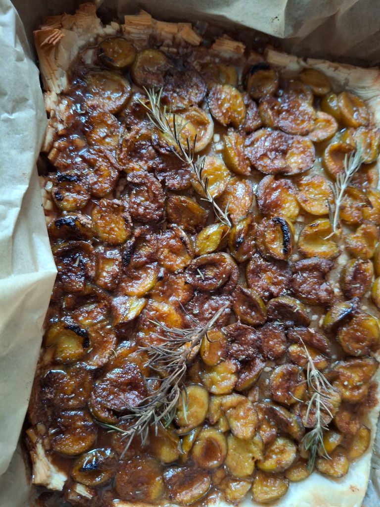 Puff pastry tart filled with small green plums and a caramelised glaze, with sprigs of rosemary