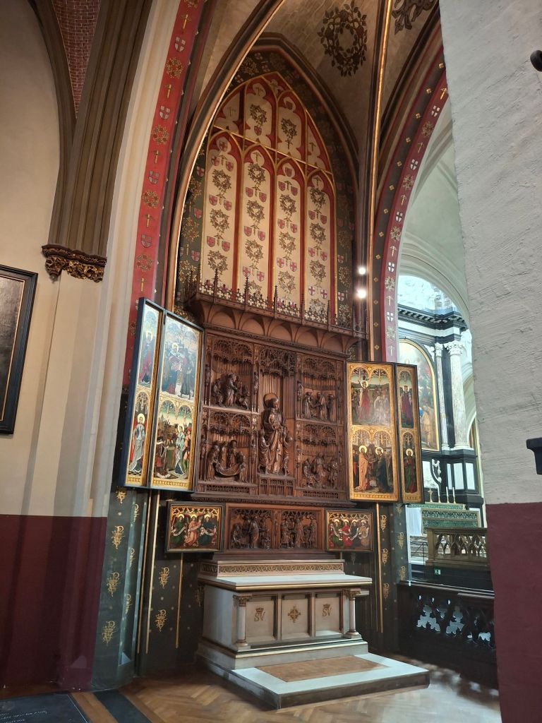 Inside a cathedral, a five-panelled painting of saints on wood behind an altar