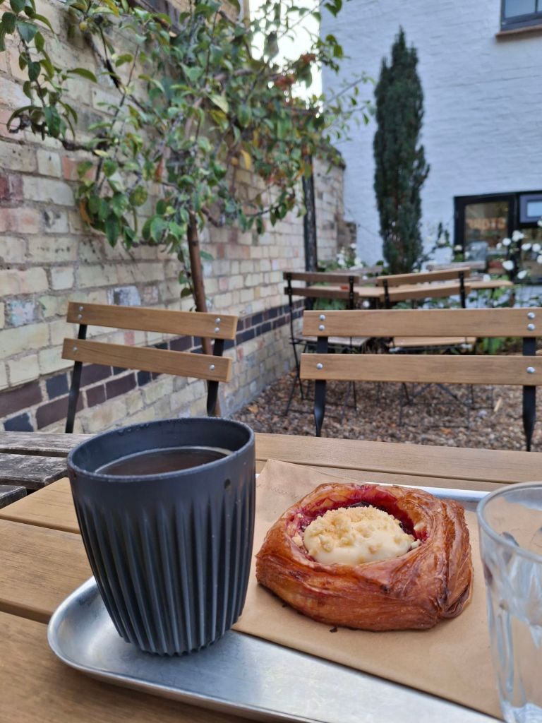 A cup of black coffee and a Danish pastry on a table in a walled garden